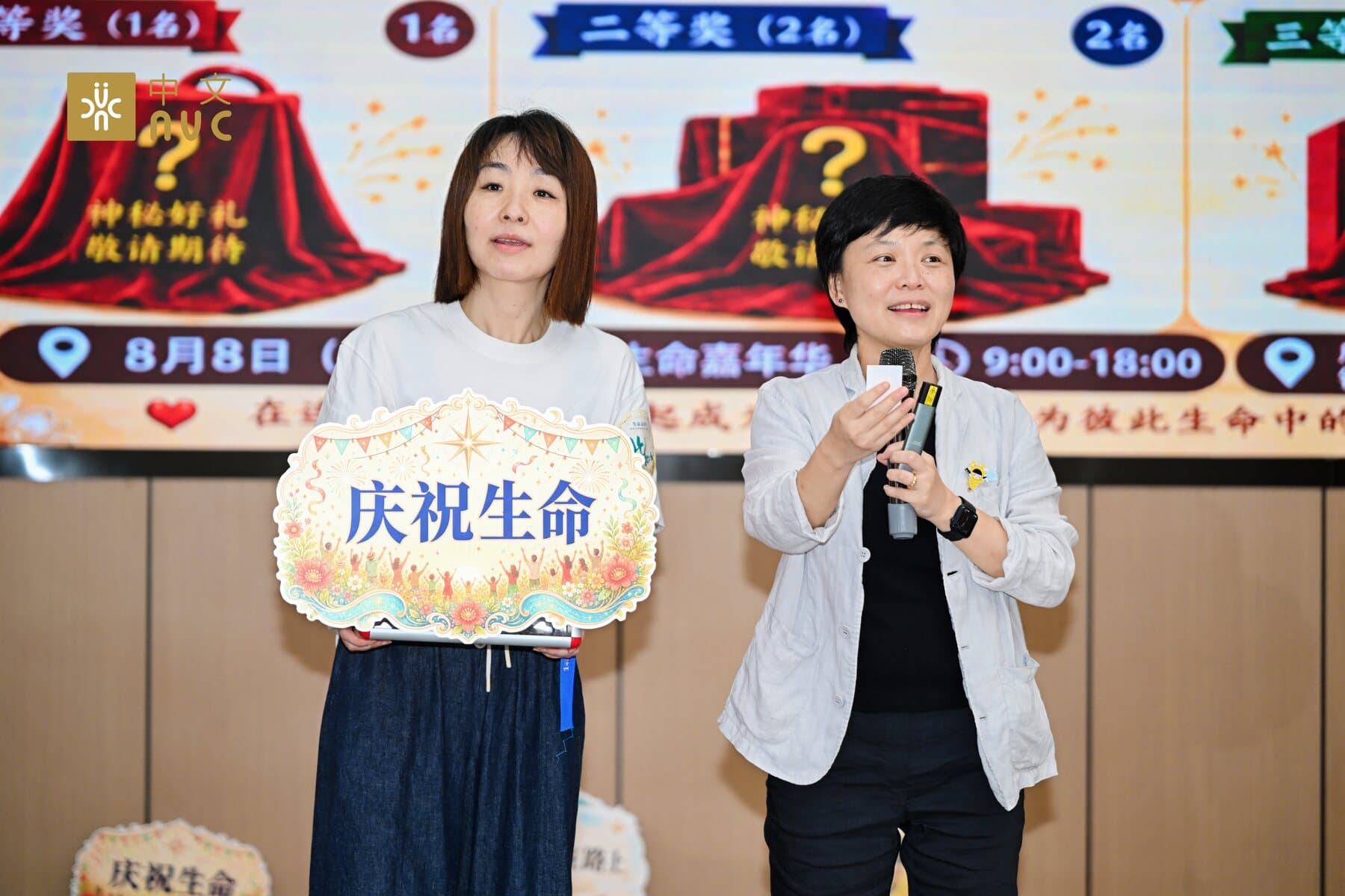 两位伙伴在成都站舞台前手持庆祝生命主题牌分享